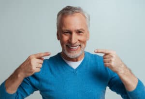 A man smiling and pointing to his teeth after being treated with a dental soft tissue laser