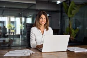 Busy professional woman sitting at her office desk smiling with Invisalign